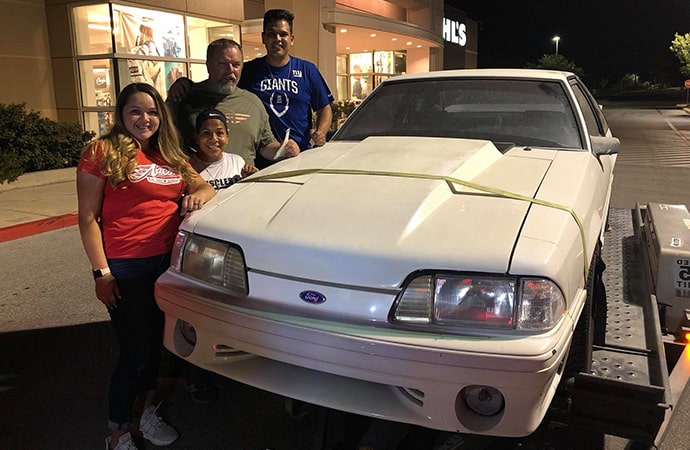 The Ryan family poses with their dad's 1993 Ford Mustang he sold 17 years ago to pay their mother's medical bills. Now cancer-free, she helped her children surprise their father with the gift. | Facebook photo