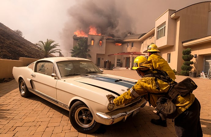 Firefighters push a vehicle from a garage as the Woolsey fire burning a home near Malibu Lake in Malibu, Calif., Friday, Nov. 9, 2018. | AP Photo/Ringo H.W. Chiu